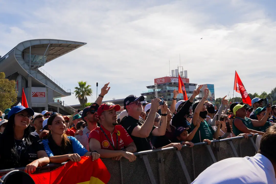 Fans at the Fan Zone barrier with Spanish flags, the Circuit grandstand and control tower behind